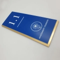 Detal personalizowanej tabliczki z numerem pokoju, logo i grawerem na niebieskim laminacie.jpg